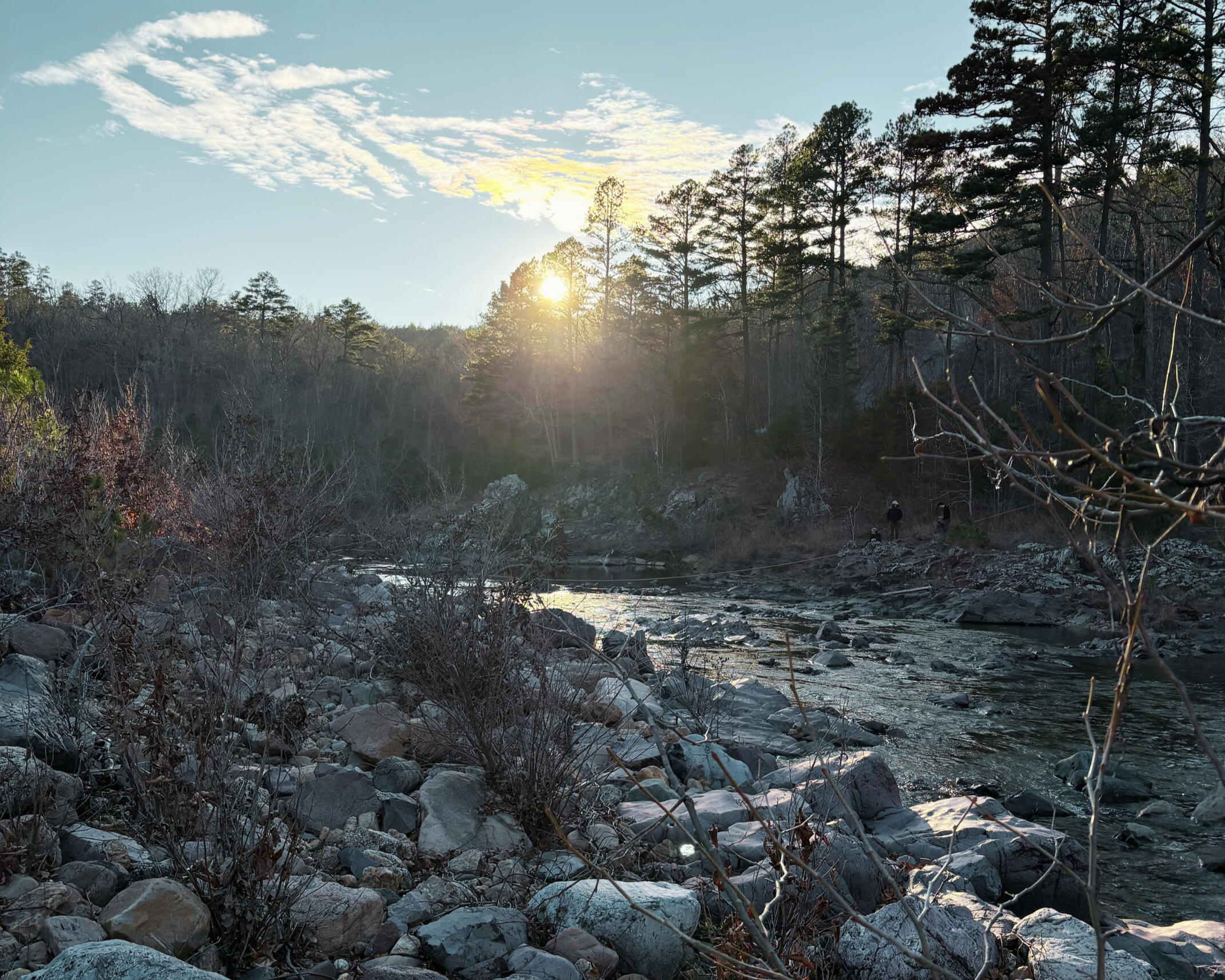 Sunset over the river in the Ozarks with the sun peaking through the pines.